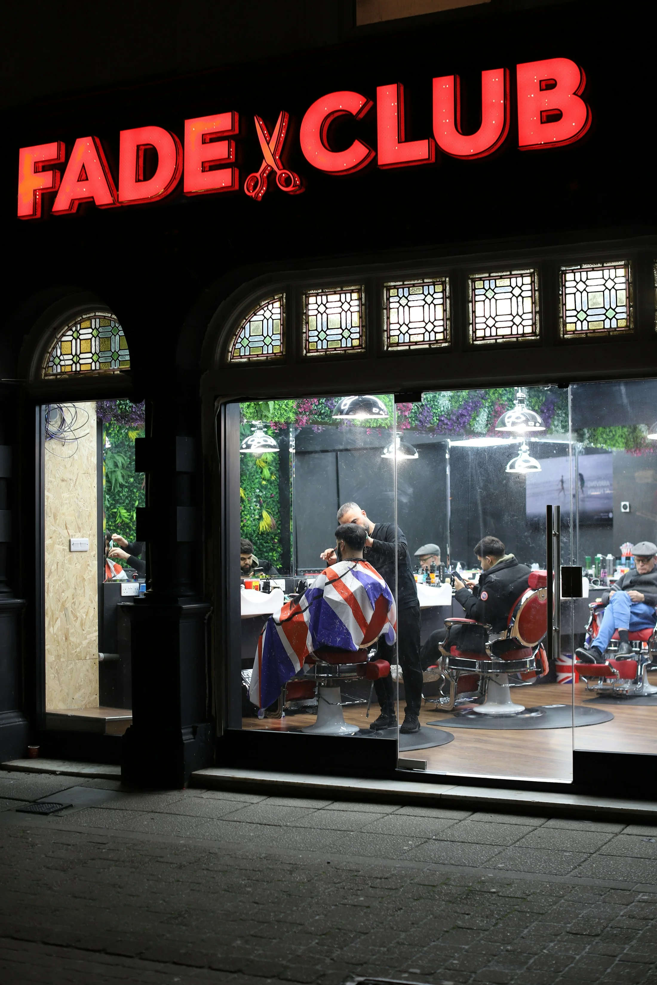 A busy barbershop seen from the street at night
